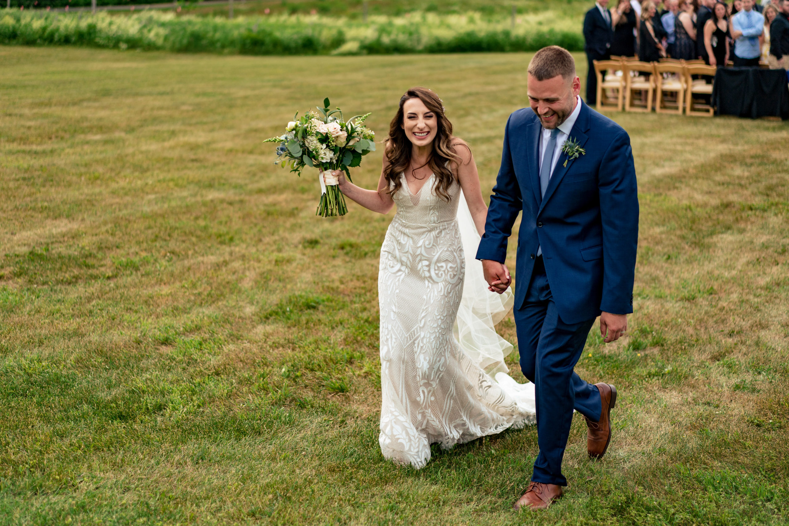 bride and groom exiting ceremony. Bride in lace dress and white flowers in bridal bouquet, groom in blue suit and brown shoes